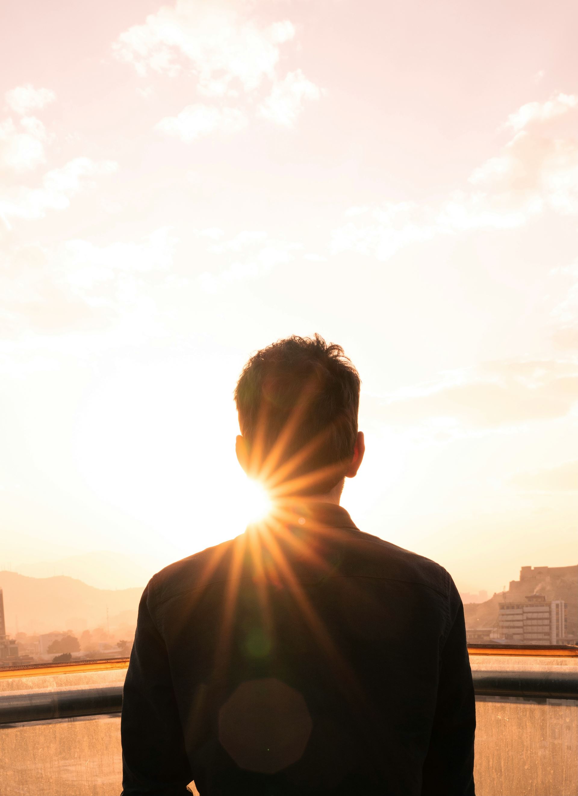 a silhouette of the back of a man's head looking at the sun setting on the horizon