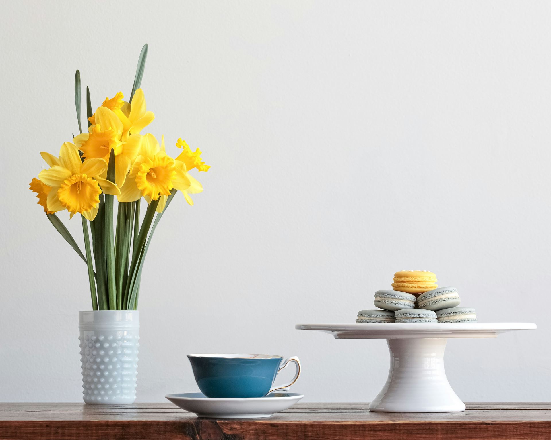 A vase of daffodils, a cup of tea and a plate of macarons